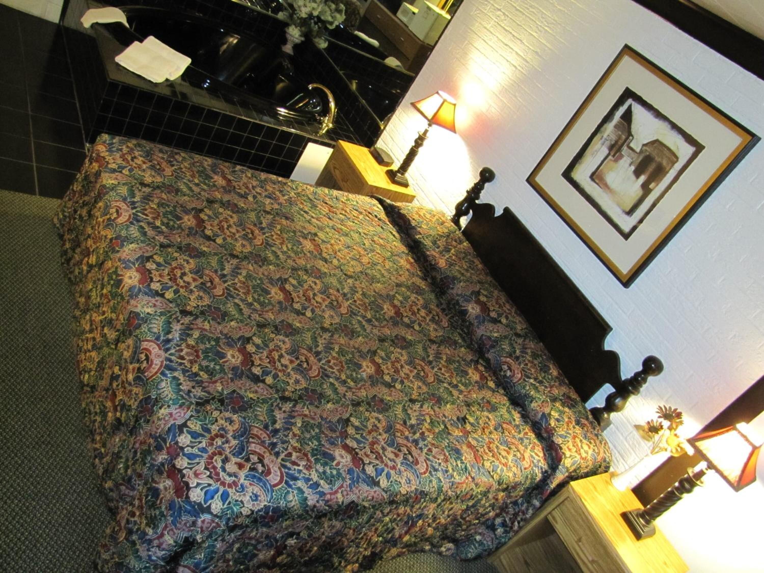 Una cama con una colcha estampada, una mesita de noche con una lámpara, y un cuadro enmarcado en la pared.