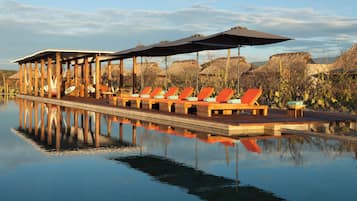 Una piscina al aire libre, sombrillas, sillones reclinables de piscina