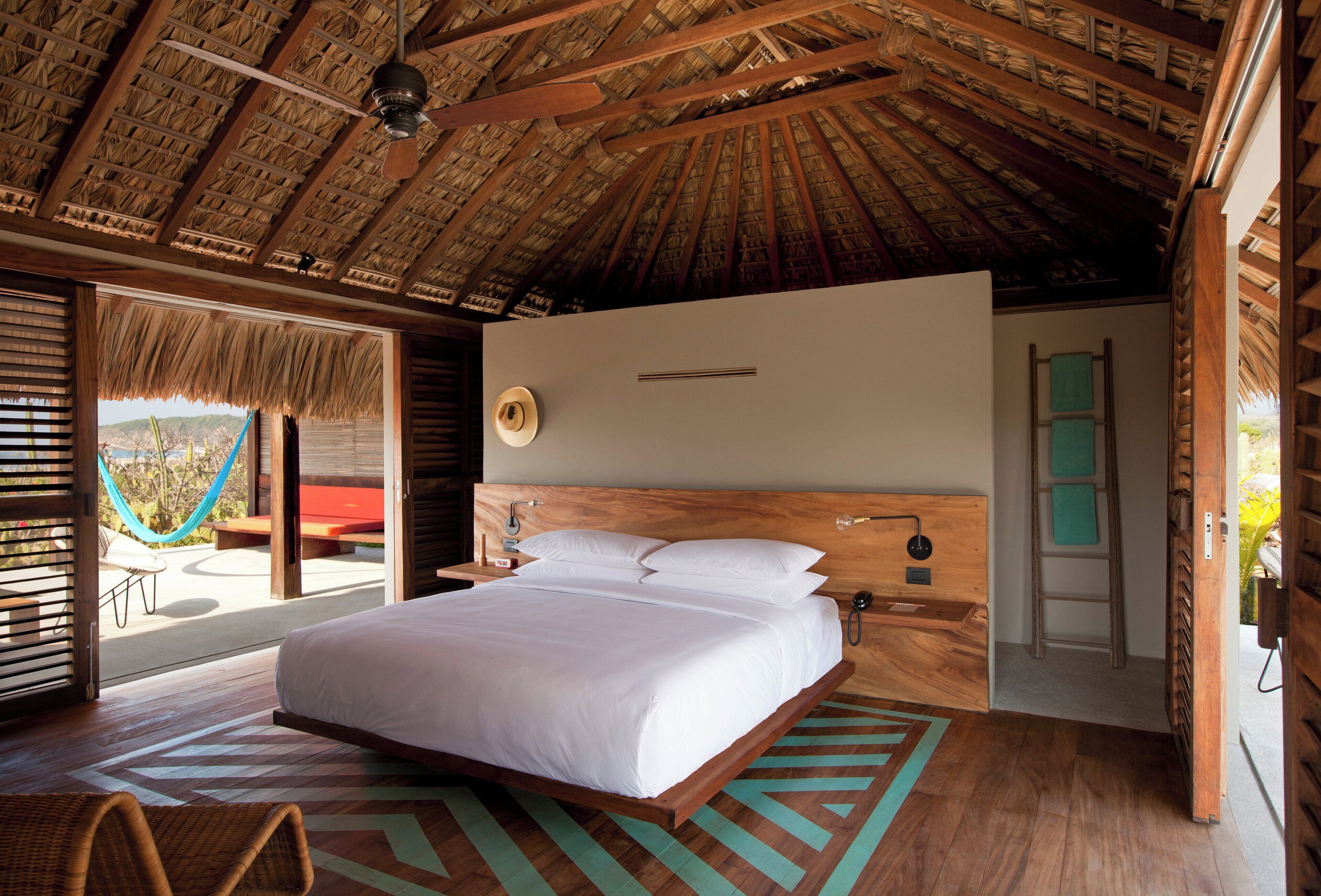 A spacious bedroom with a large bed, wooden headboard, and a view of a hammock outside.