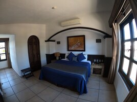 Un dormitorio con una cama grande, techo abovedado, un cuadro y una ventana con cortinas.