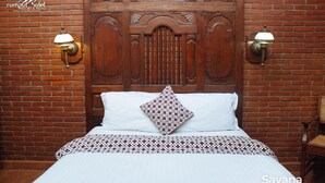 Habitación de hotel con cabecera de madera, dos lámparas fijadas a la pared, colcha estampada y una almohada decorativa.