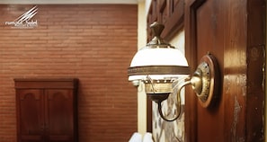 Una lámpara de pared de bronce con pantalla blanca, fijada a una puerta de madera con pomo de bronce.