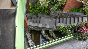 Un pequeño jardín al aire libre con un sendero de piedra, una fuente ornamental y diversas plantas.