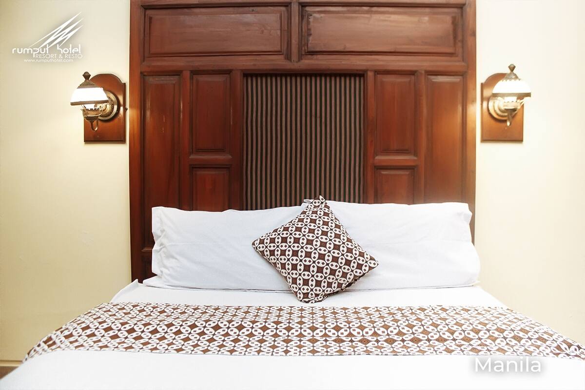 A hotel room with a wooden headboard, two wall-mounted lights, a patterned bedspread, and a decorative pillow.
