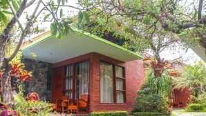 Una casa de ladrillo con techo verde, ventanas grandes y un jardín con diversas plantas y un camino.
