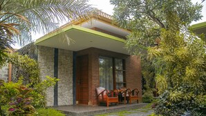 Una casa moderna con fachada de piedra y ladrillo, un porche cubierto con mobiliario de madera y un jardín cuidado con piedras para caminar.