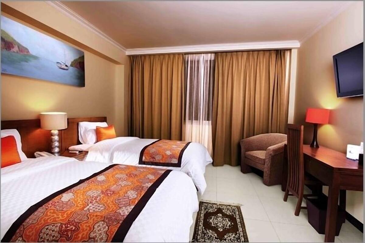 Habitació d'hotel amb dos llits, una taula de treball, una cadira, televisió i un quadre penjat a la paret.