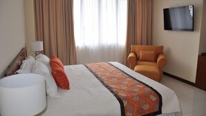 A hotel room with a bed, a chair, a TV, and curtains. - Dermaga Keluarga Hotel (Yogyakarta)