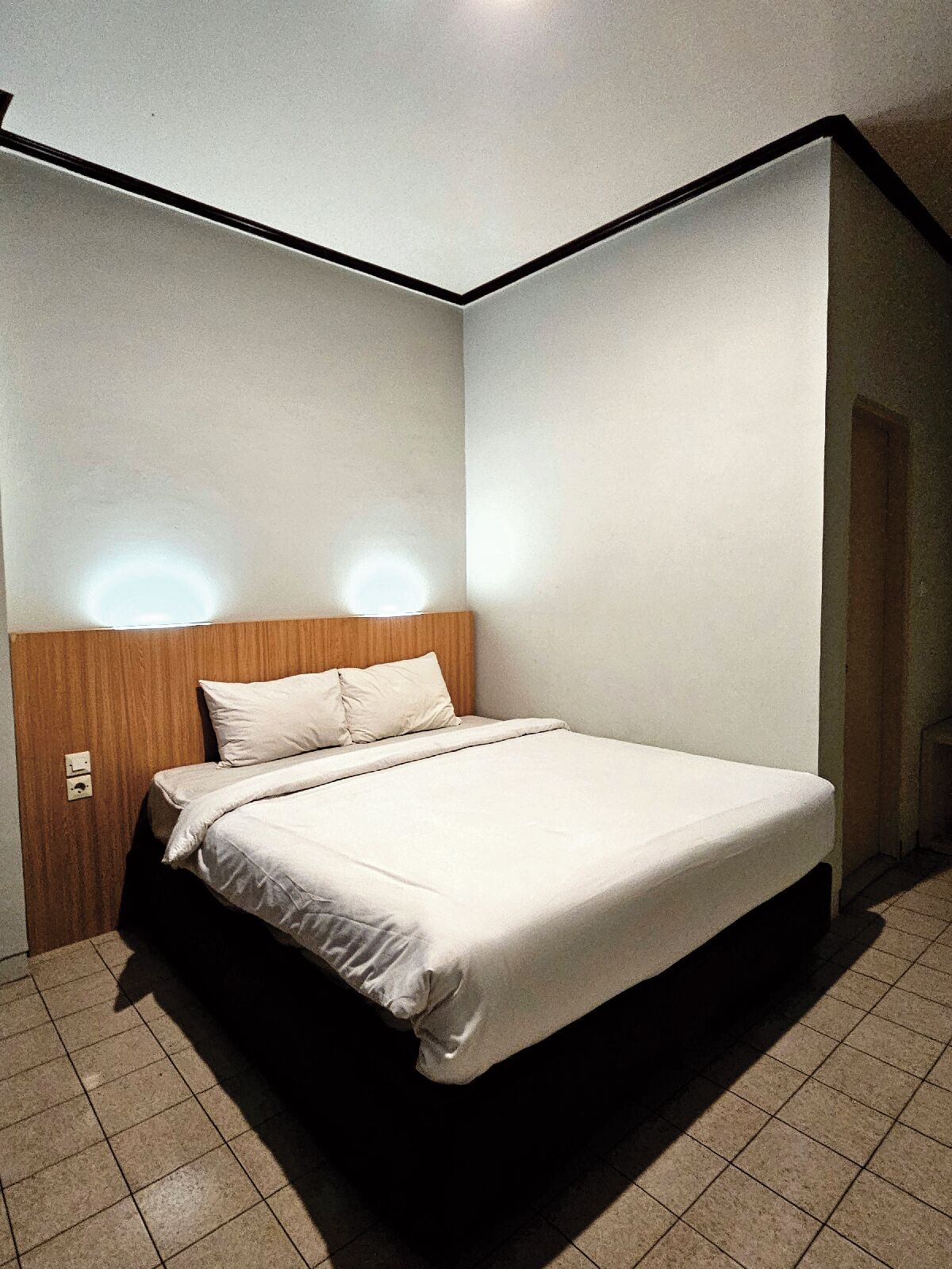 A single-bed room with a wooden headboard, white bedding, and a tiled floor.