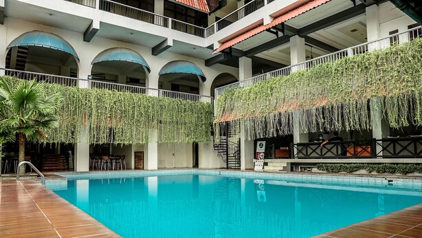 A pool with a wooden deck, surrounded by a multi-level building with balconies and arches. - Airlangga Hotel (Yogyakarta)