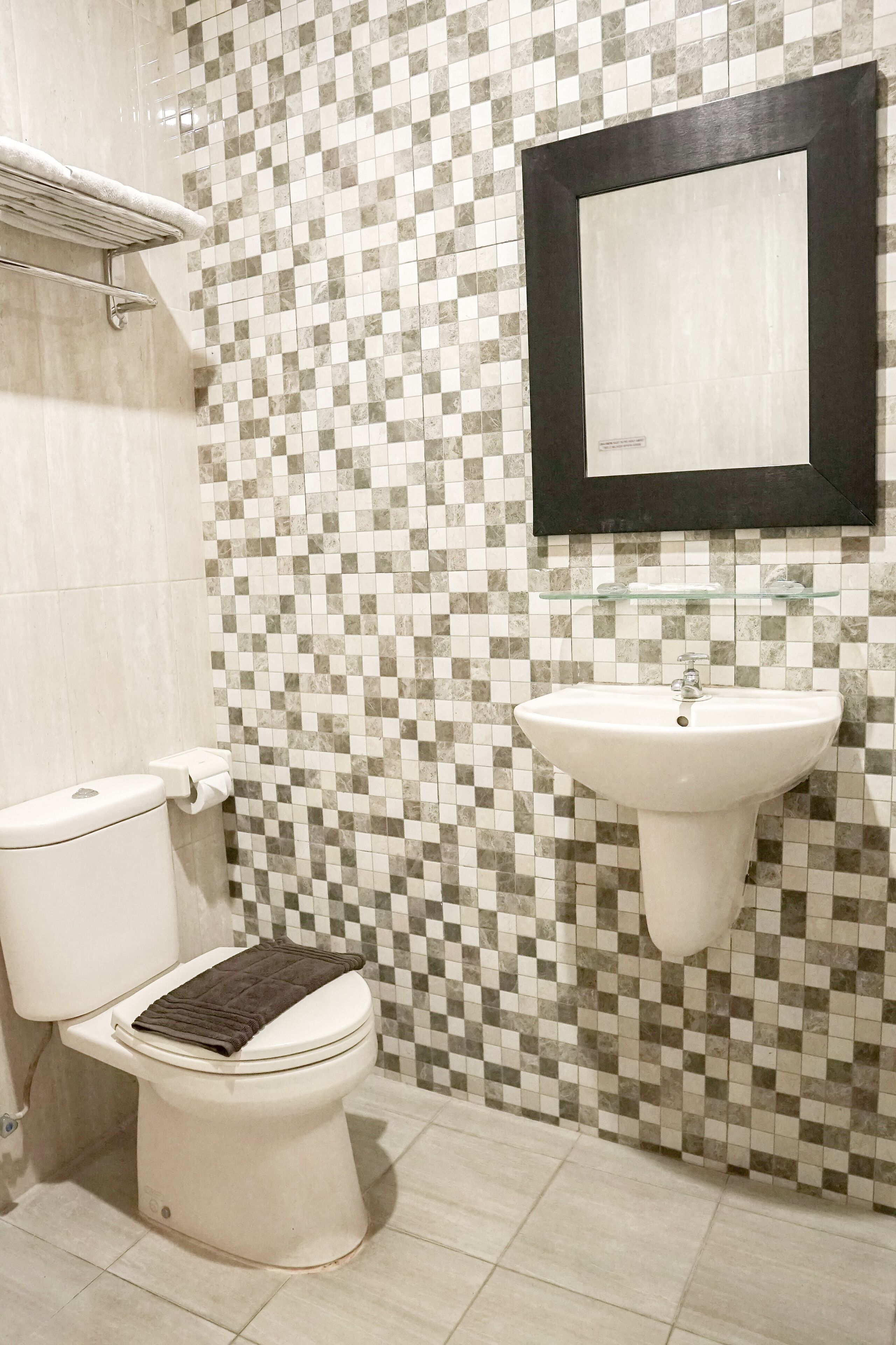A bathroom with a tiled floor, a toilet, a sink, and a mirror.