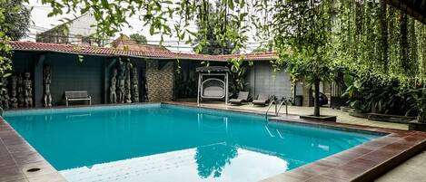 A rectangular swimming pool with a tiled deck, surrounded by stone walls and a covered seating area.