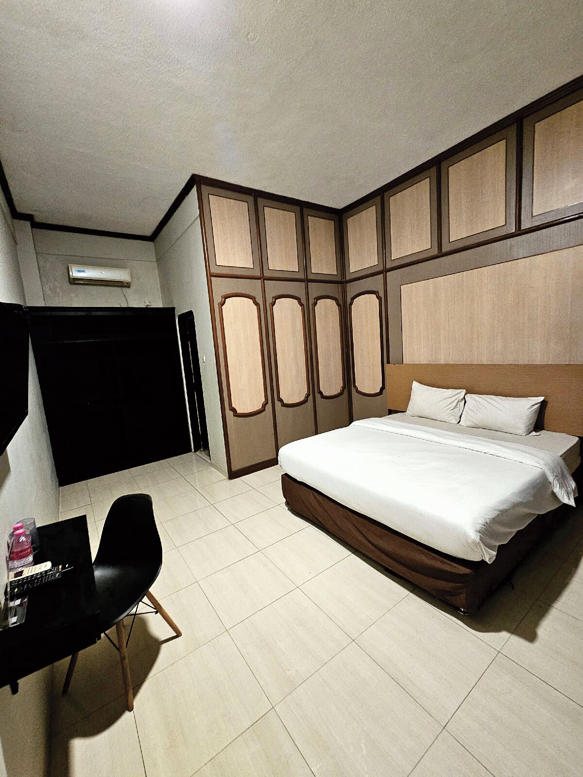 A hotel room with a large bed, a desk with a chair, and a wardrobe.