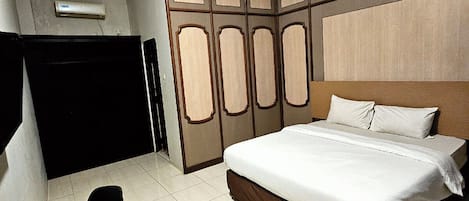 A hotel room with a large bed, a desk with a chair, and a wardrobe.