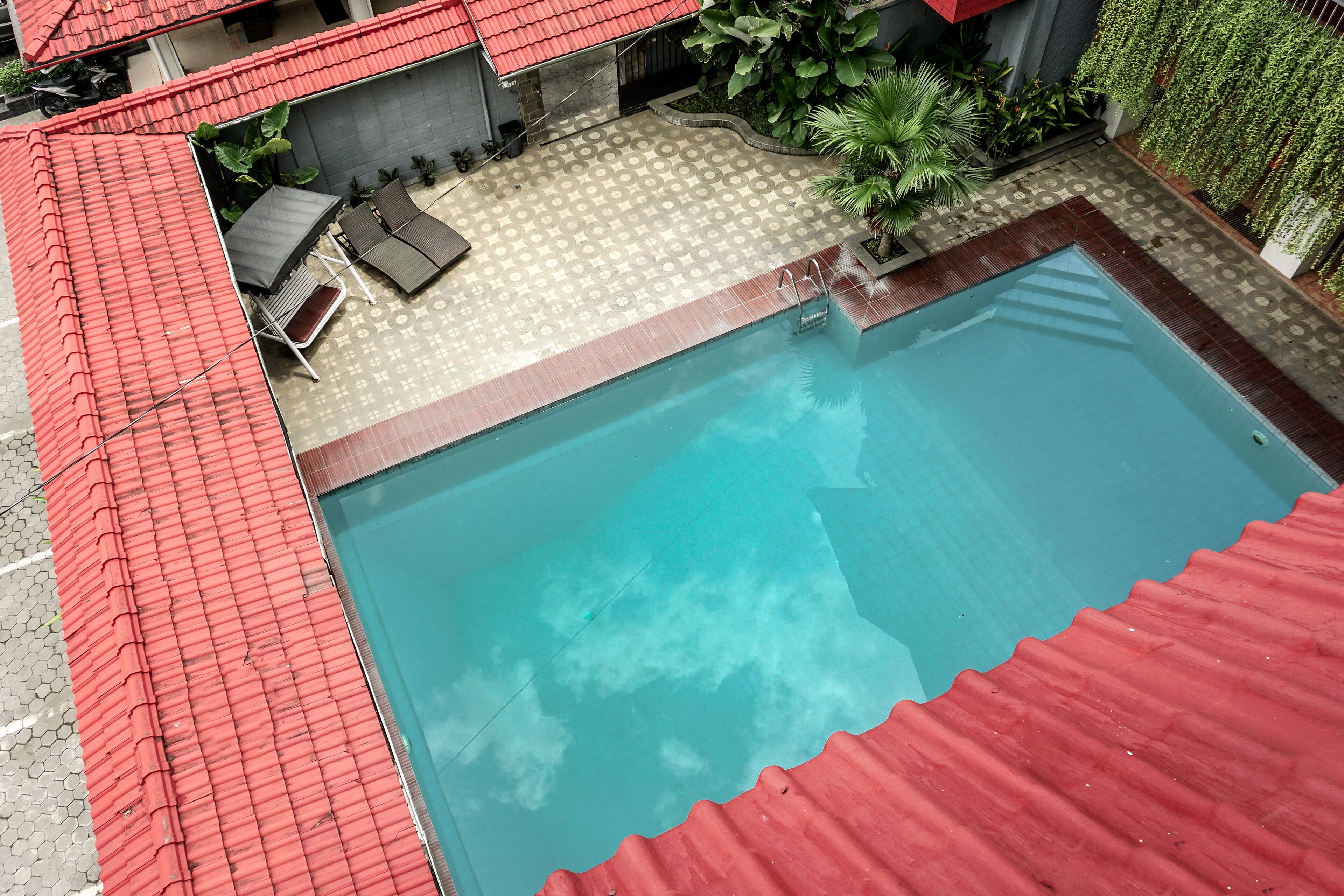 A swimming pool with a red roof, a tiled deck, and a small seating area with a table and chairs.