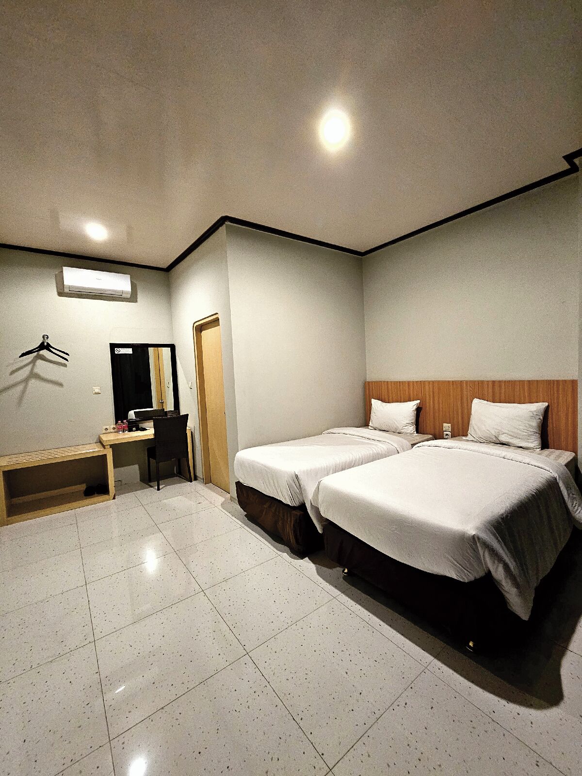 Habitación de hotel con dos camas, un escritorio, una silla, un espejo y un armario.