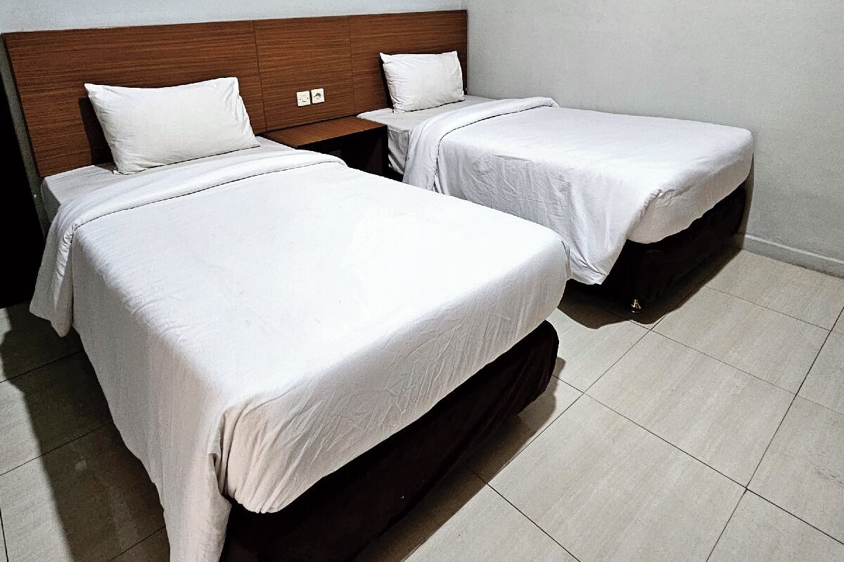 Ett hotellrum med två separata sängar, en sänggavel i trä och ett klinkergolv.