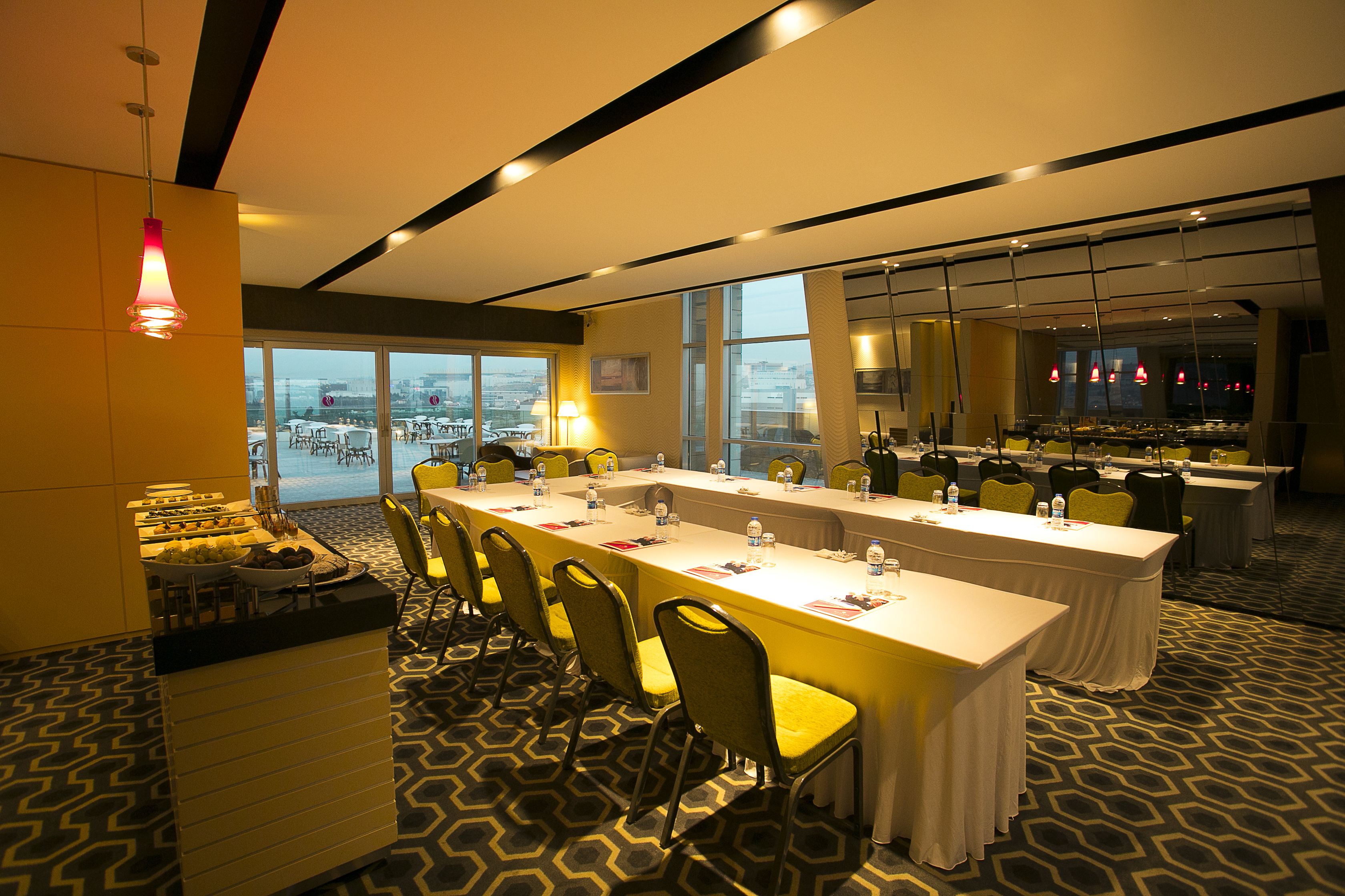 Een vergaderzaal met een lange tafel, stoelen en een buffet.