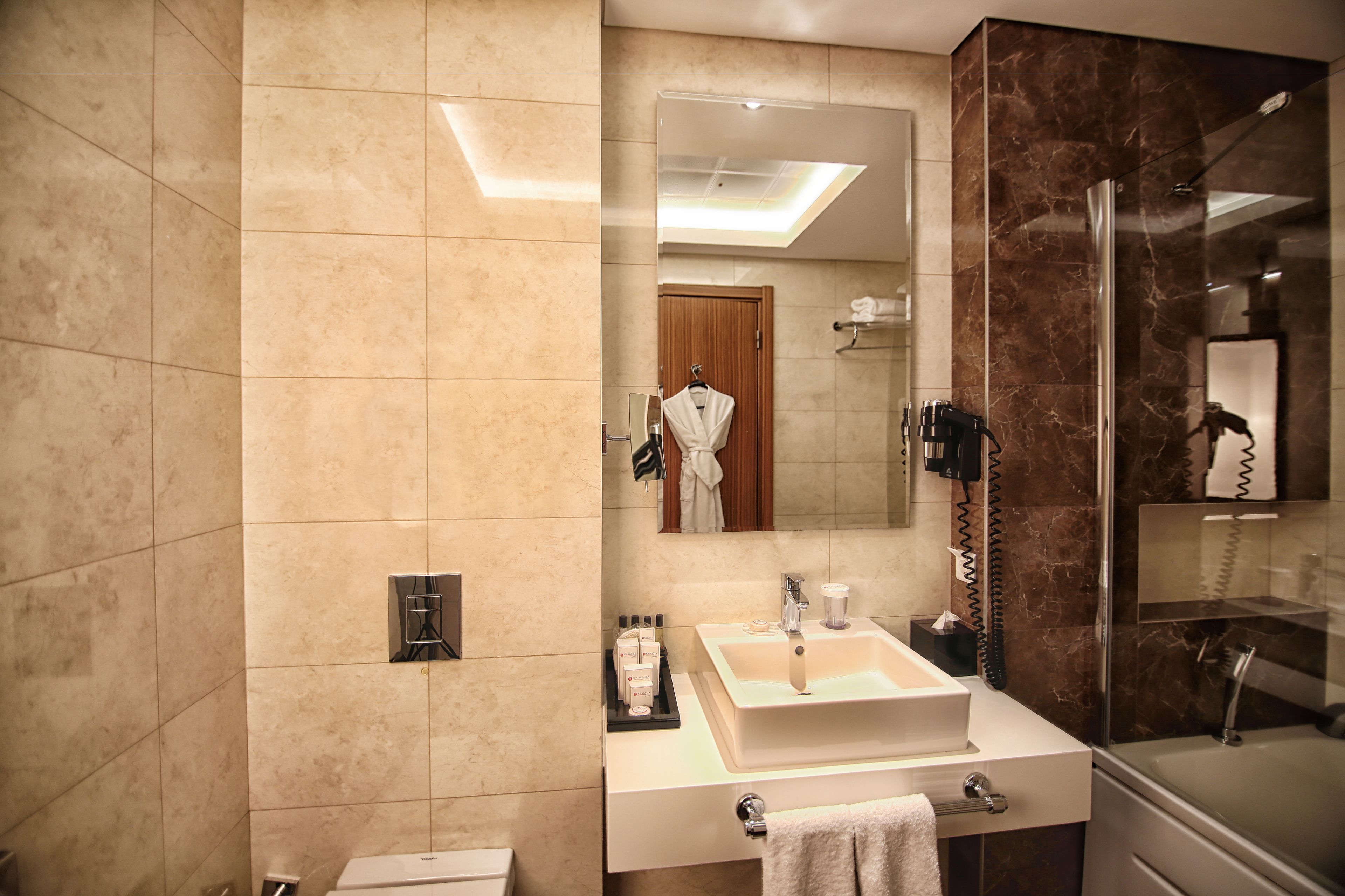 Un baño moderno con un espejo grande, un lavamanos con toallero, cabina de ducha con mampara de vidrio y tocador con artículos de aseo.