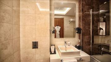 Un baño moderno con un espejo grande, un lavamanos con toallero, cabina de ducha con mampara de vidrio y tocador con artículos de aseo.