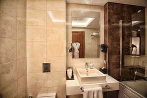 Et moderne badeværelse med et stort spejl, en vask med håndklæderadiator, en brusekabine i glas og et toiletbord med toiletartikler.