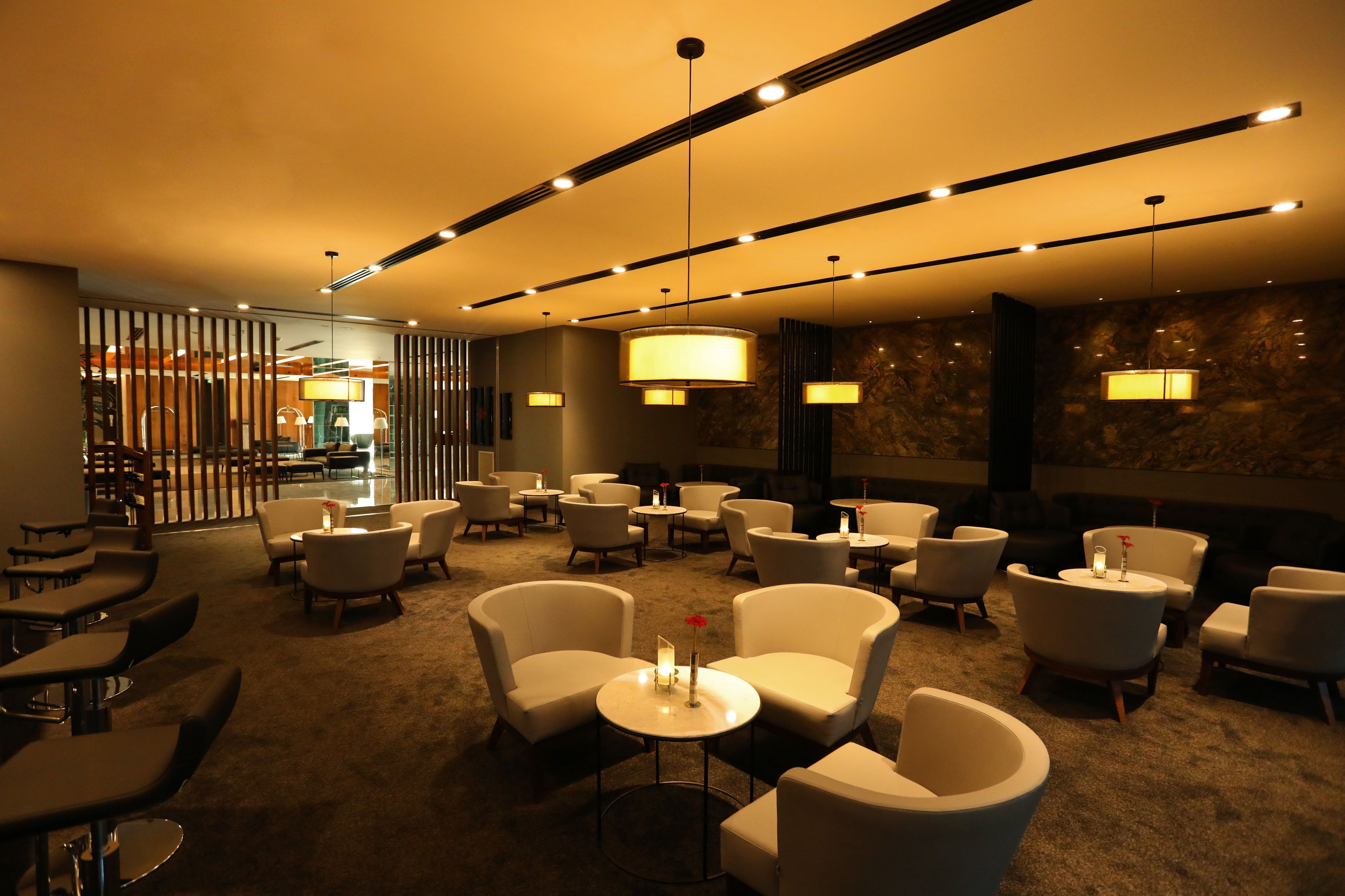 A modern lounge area with multiple seating options, including sofas and armchairs, arranged around a central table with a vase and candle.