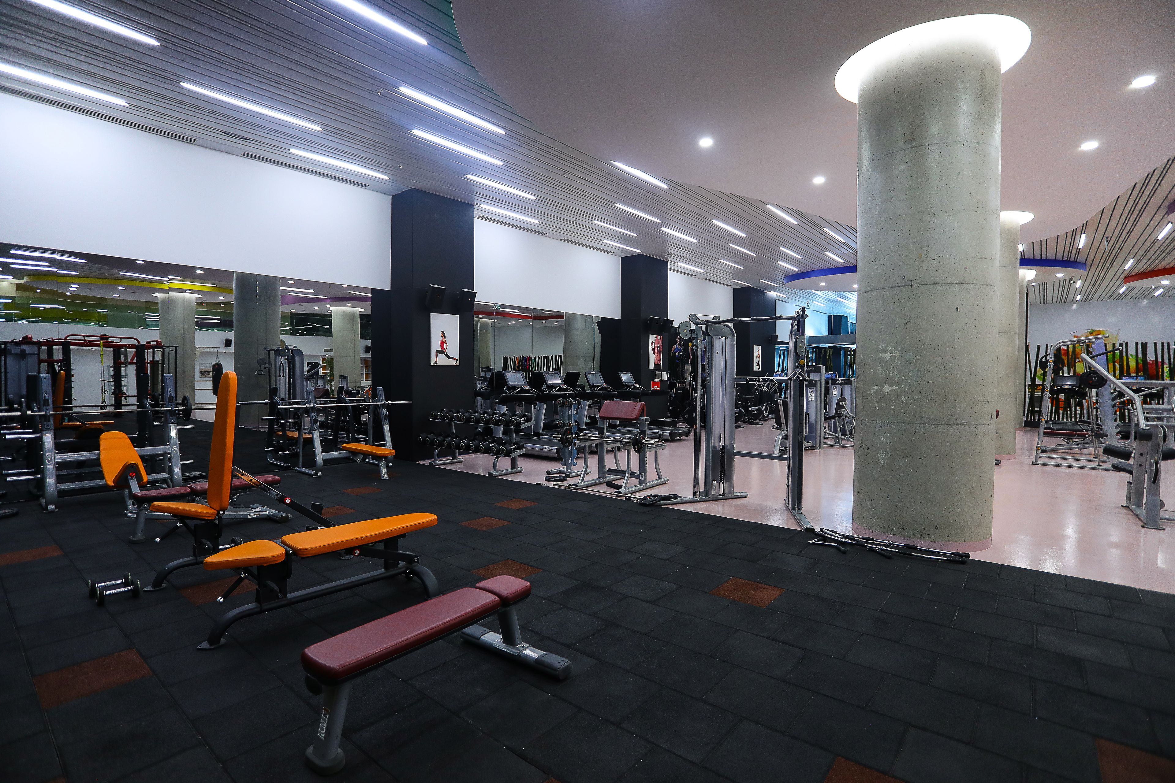 Une salle de sport équipée de divers appareils d’exercice, de bancs et d’une grande colonne.