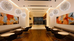 Un salón moderno con un área de estar central, mesas redondas y arte abstracto en las paredes.