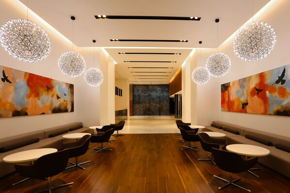 A modern lounge with a central seating area, round tables, and abstract art on the walls.