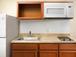 A kitchen with a built-in microwave, a stainless steel sink, and wooden cabinets. - WoodSpring Suites Chesapeake - Norfolk Greenbrier (Chesapeake)
