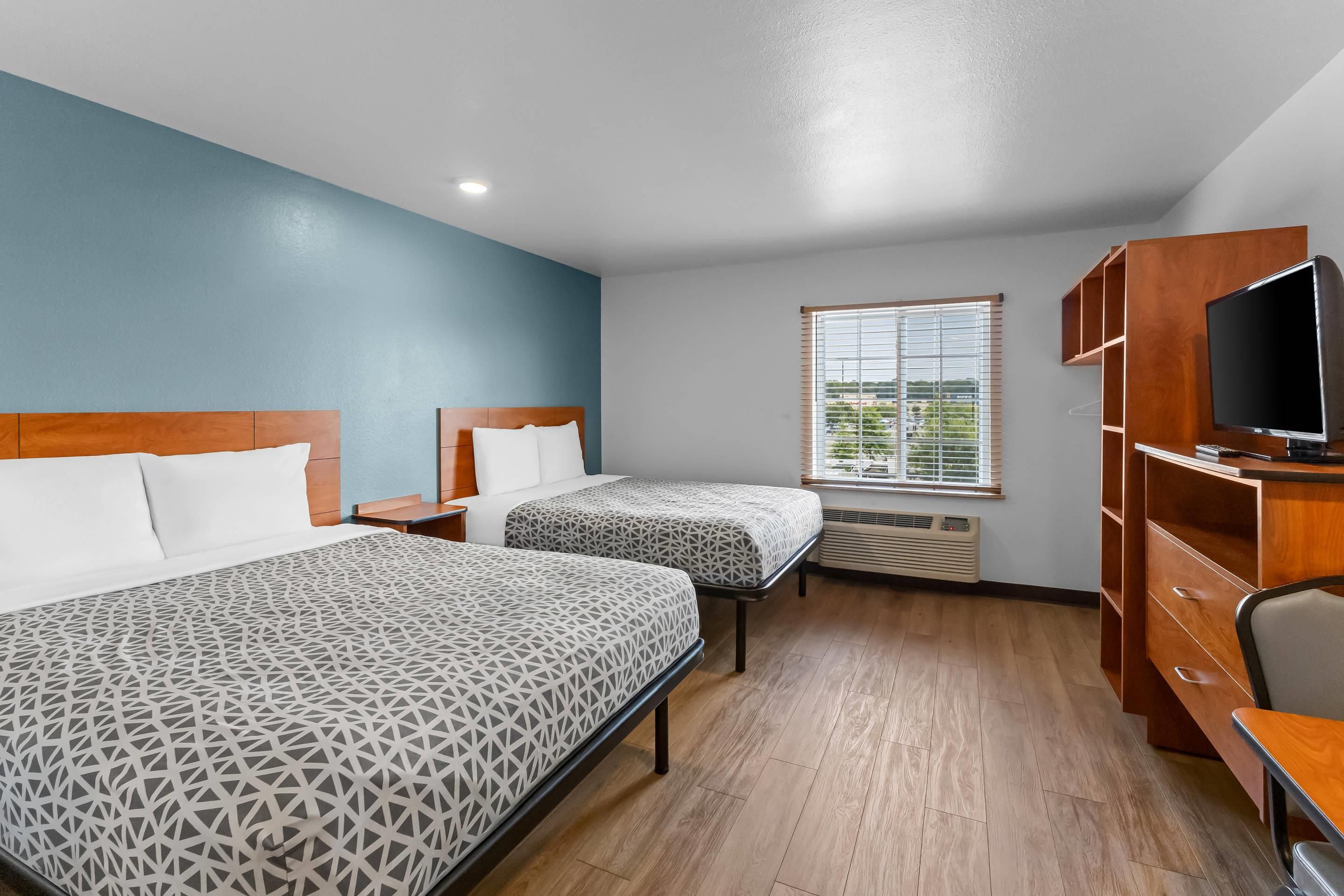 A hotel room with two beds, a TV, and a window with blinds.
