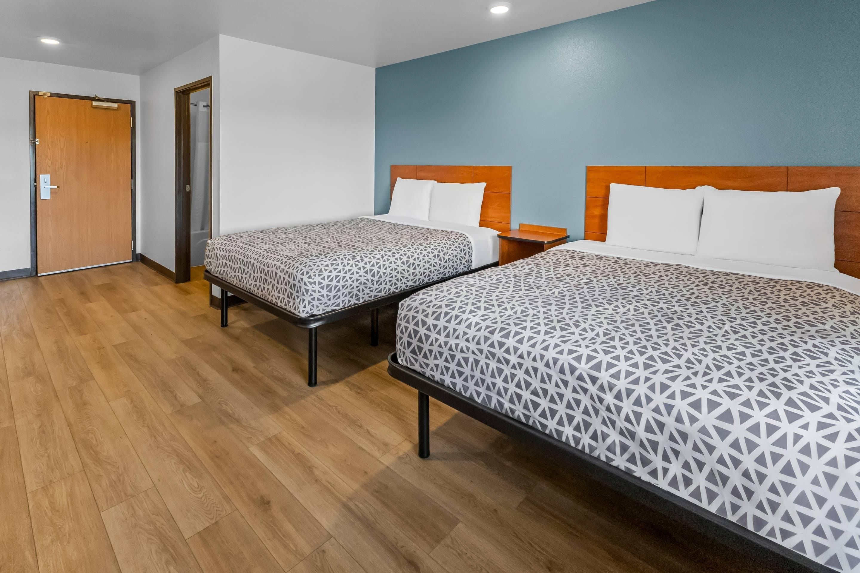 A hotel room with two beds, wooden flooring, and a blue accent wall.