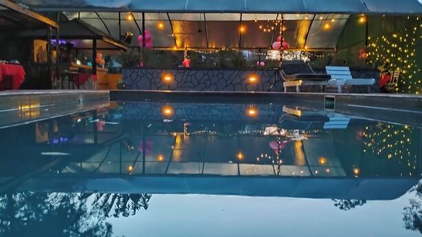 A pool area with a glass enclosure, string lights, and a stone wall. - Hotel Troy (Nairobi)