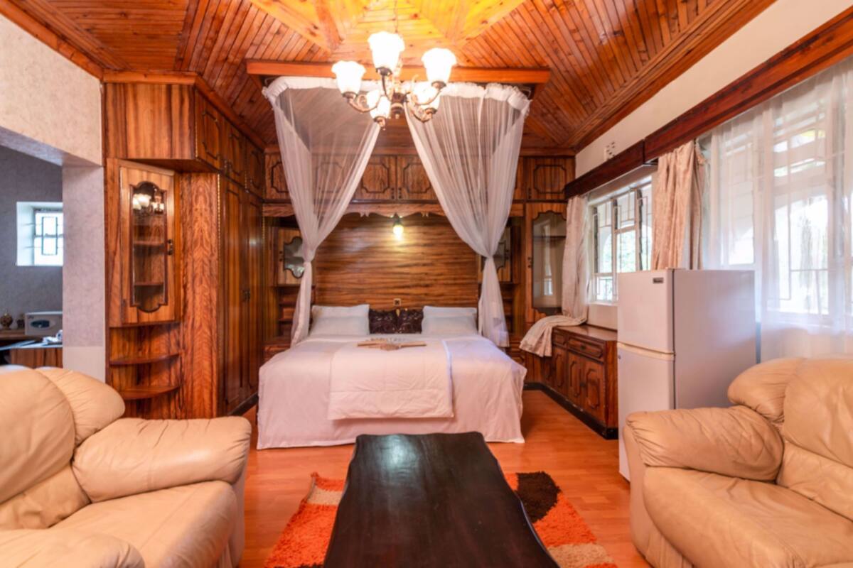 A wooden cabin-style bedroom with a bed, two leather chairs, a nightstand, and a chandelier.