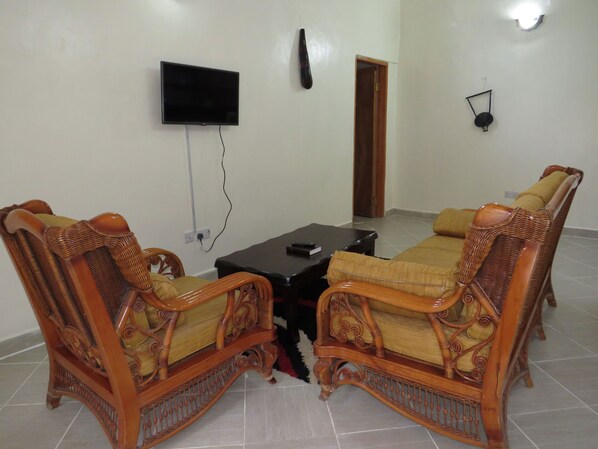 Una sala de estar con dos sillas de madera, una mesa de centro negra y un televisor de pantalla plana montado en la pared.