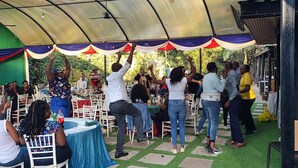 A covered outdoor event area with tables and chairs, some people standing and others seated. - Hotel Troy (Nairobi)