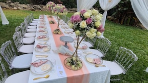 A long table set outdoors with clear chairs, white tablecloth, and floral centerpieces. - Hotel Troy (Nairobi)