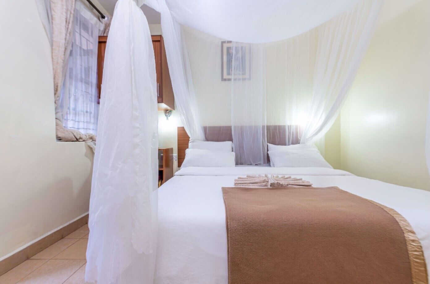 A bedroom with a bed, white curtains, a brown blanket, and a canopy.