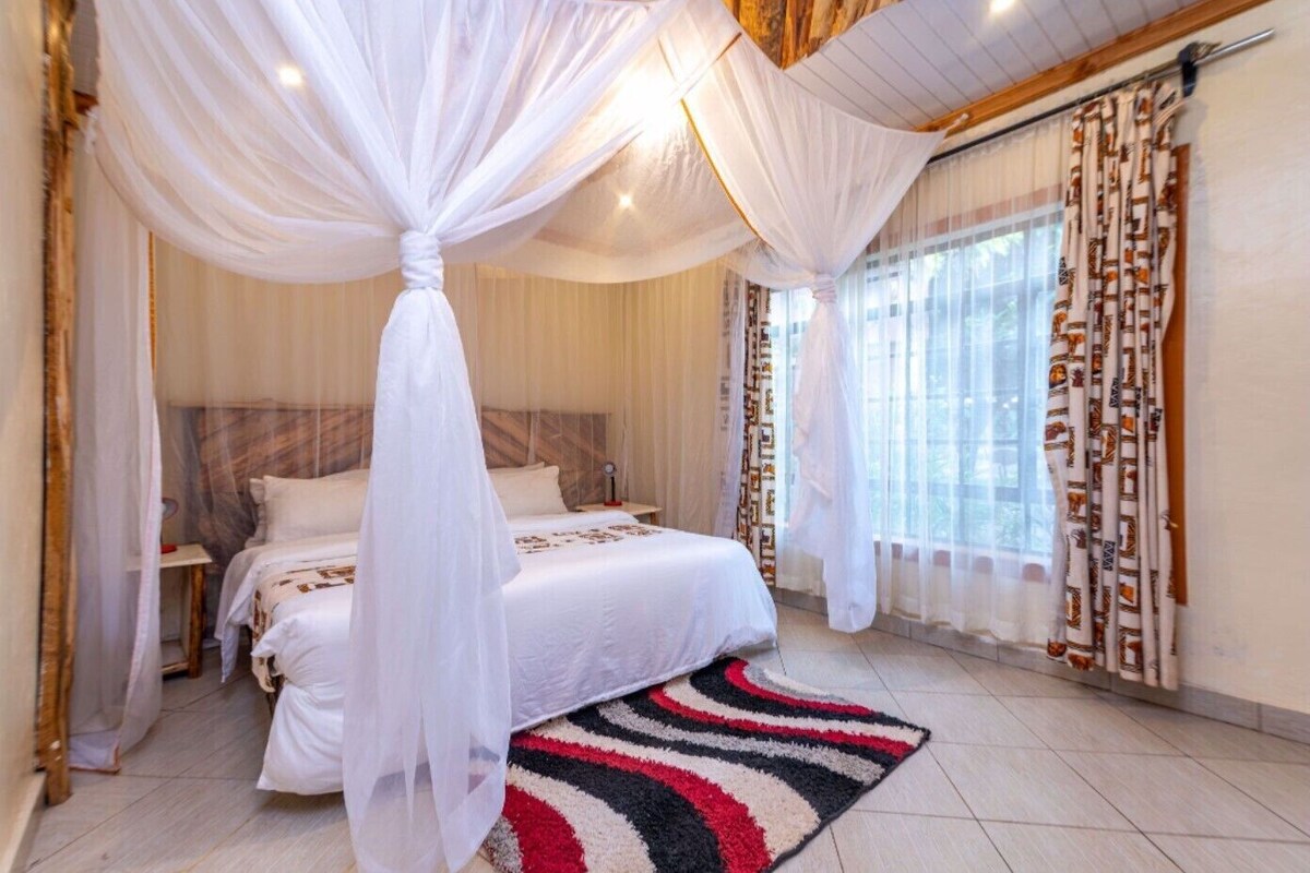A bedroom with a bed, a nightstand, a bedside table, a window with curtains, and a patterned rug.