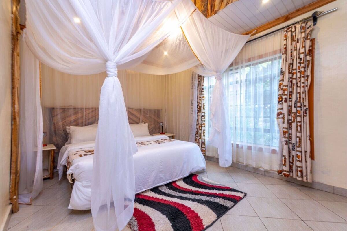 A bedroom with a bed, a nightstand, a bedside table, a window with curtains, and a patterned rug.