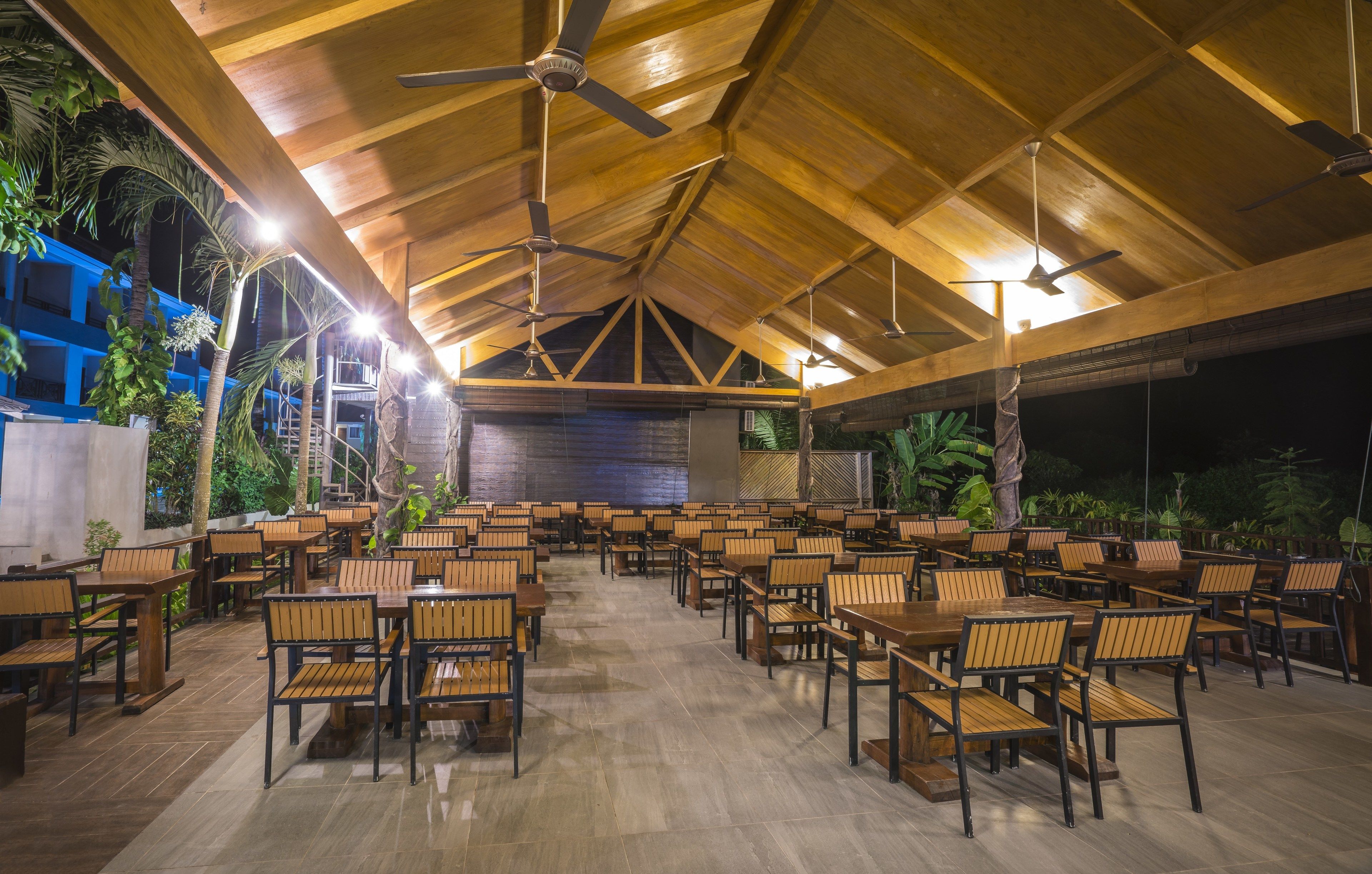 Un espace de restauration intérieur avec des tables et des chaises en bois, des ventilateurs de plafond et un sol carrelé.