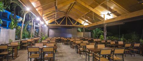 Un espace de restauration intérieur avec des tables et des chaises en bois, des ventilateurs de plafond et un sol carrelé.