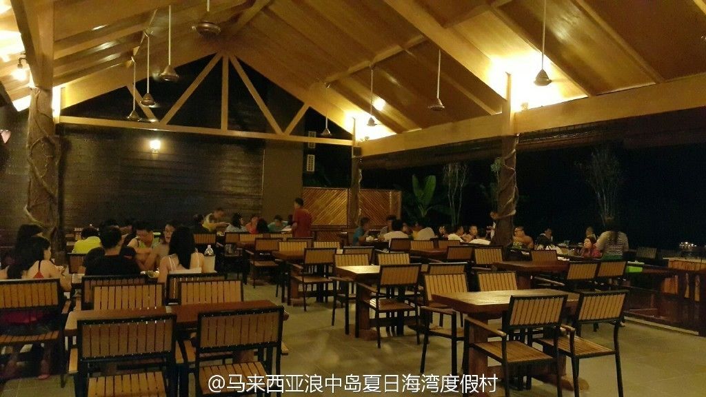 An indoor dining area with wooden tables and chairs, a high ceiling with exposed beams, and a dark background.