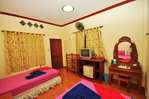 Una habitación con cama, escritorio con televisor, espejo y ventilador.