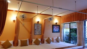 Una habitación con una sofá cama, dos ventiladores de pared, un cartel del cuerpo humano y una ventana con cortinas.