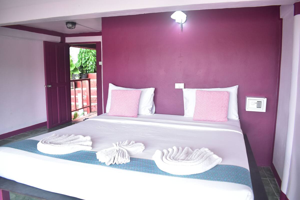 A neatly made bed with white and pink linens, a blue and white patterned bedspread, and two white towels folded on the bed.
