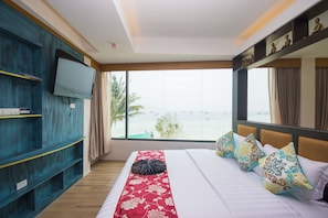 Habitación de hotel con un ventanal grande, una cama con muchas almohadas, un televisor en la pared y un mueble de madera.