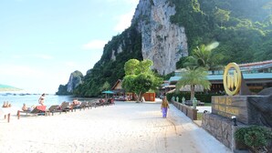 A beach with sun loungers, a large rock formation, and a hotel sign. - Phi Phi Nice Beach Hotel Hip (Ko Phi Phi)