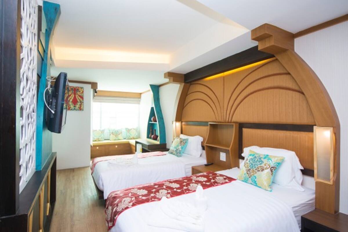 A hotel room with two beds, a TV, a window with curtains, and a decorative wall panel.
