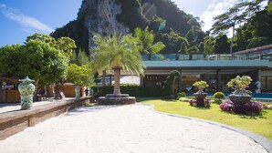 A resort with a sandy pathway, palm trees, and a mountain backdrop. - Phi Phi Nice Beach Hotel Hip (Ko Phi Phi)